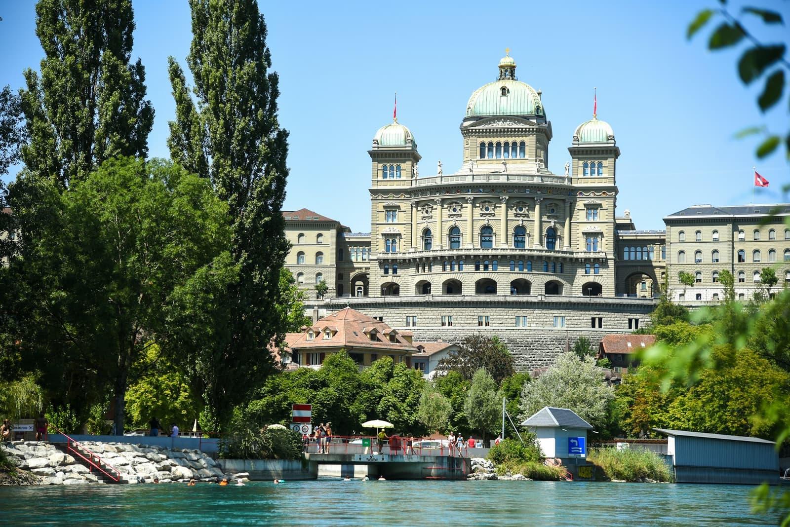 The Swiss Federal Palace in Bern seen across the Aare, the Swiss flag flying beside it.