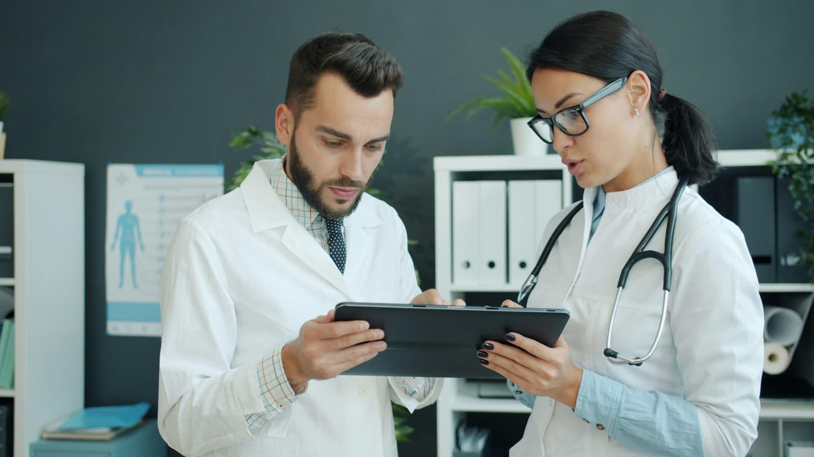 Two clinicians in white coats reviewing a patient record together on a tablet.