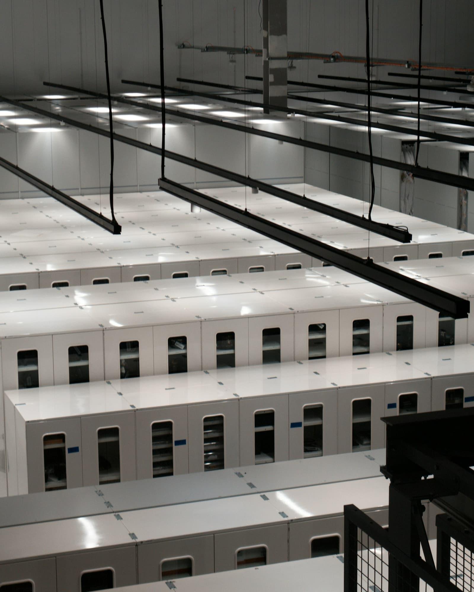 Rows of enclosed white server cabinets in a data centre hall, viewed from above.