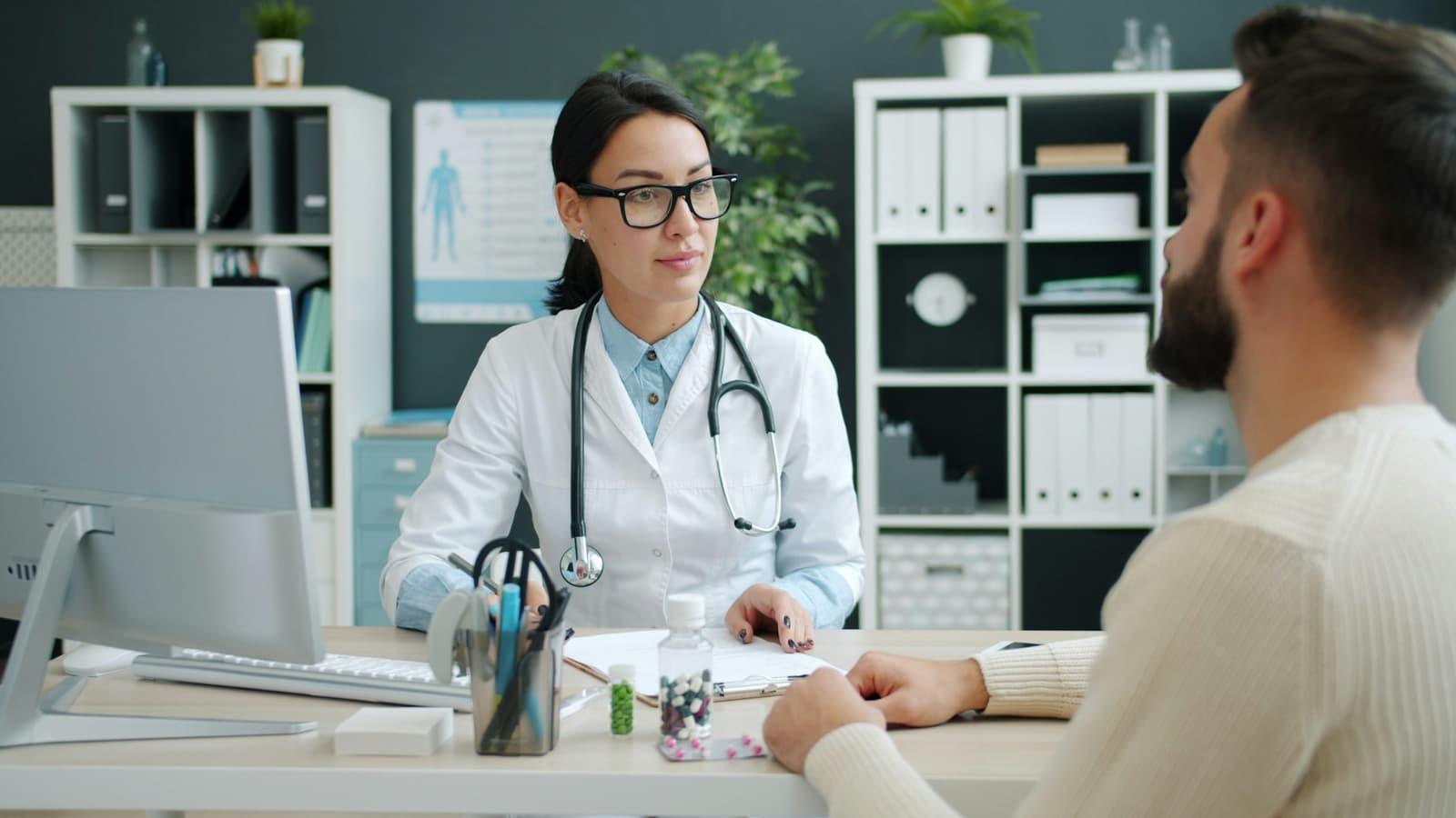 A physician in consultation with a patient across a desk in a clinic office.