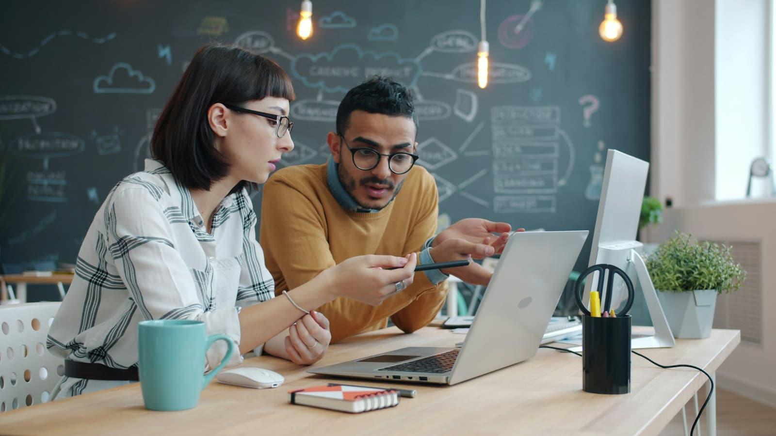 Two colleagues working through a problem together at a laptop.