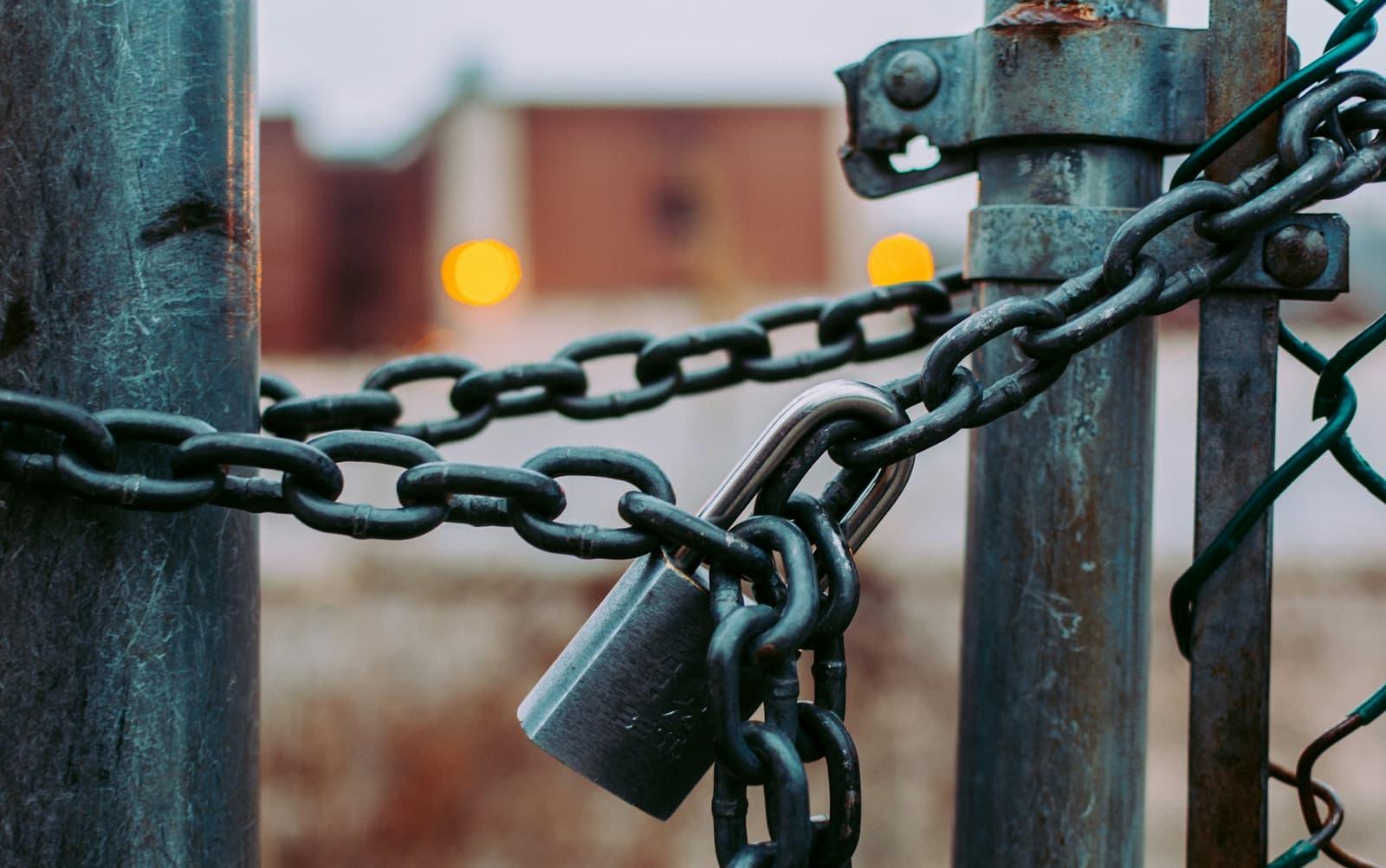 A steel padlock closing a heavy chain across a gate.