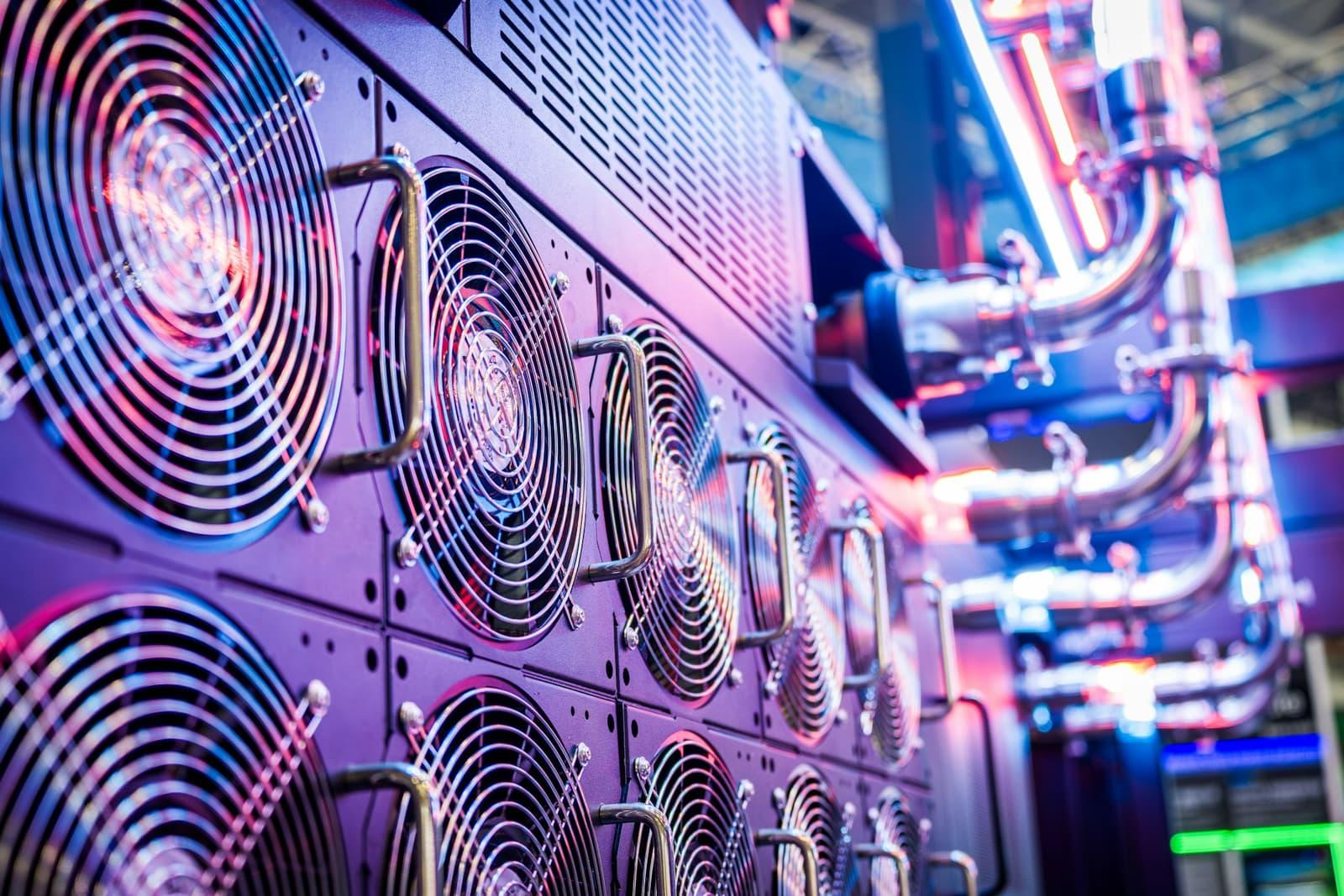 A wall of cooling fans and coolant pipework along a data centre plant room.