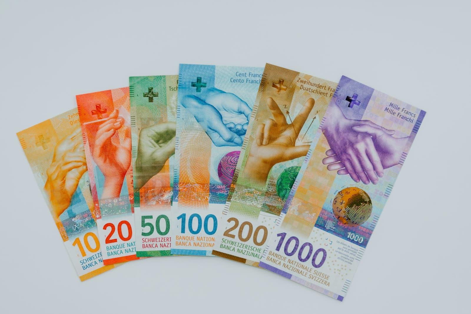 Swiss franc banknotes from ten to one thousand fanned out on a pale surface.