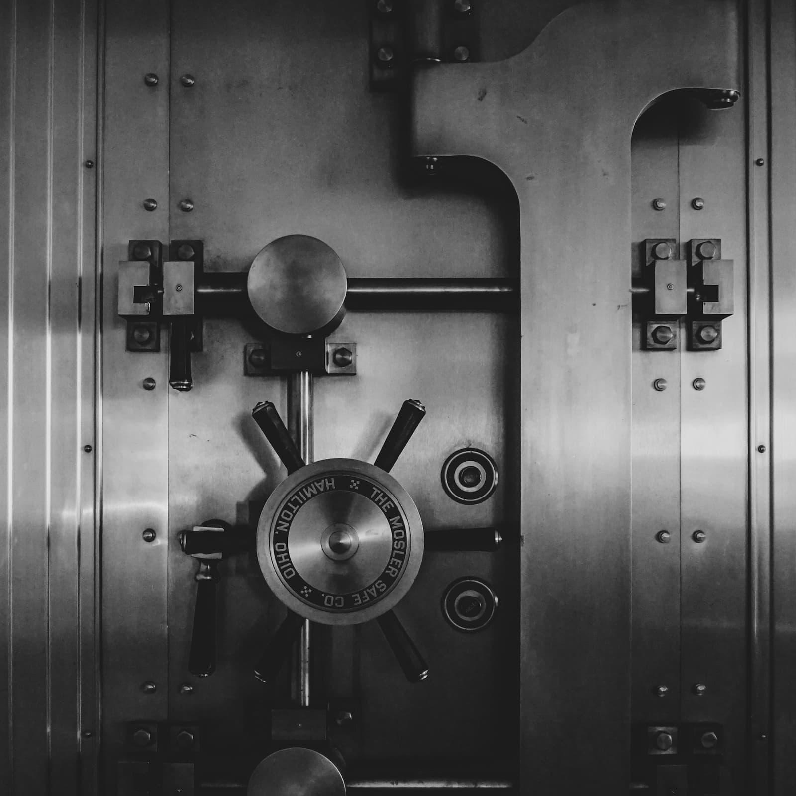 The steel door of a bank vault, closed, with its locking wheel and bolt work exposed.