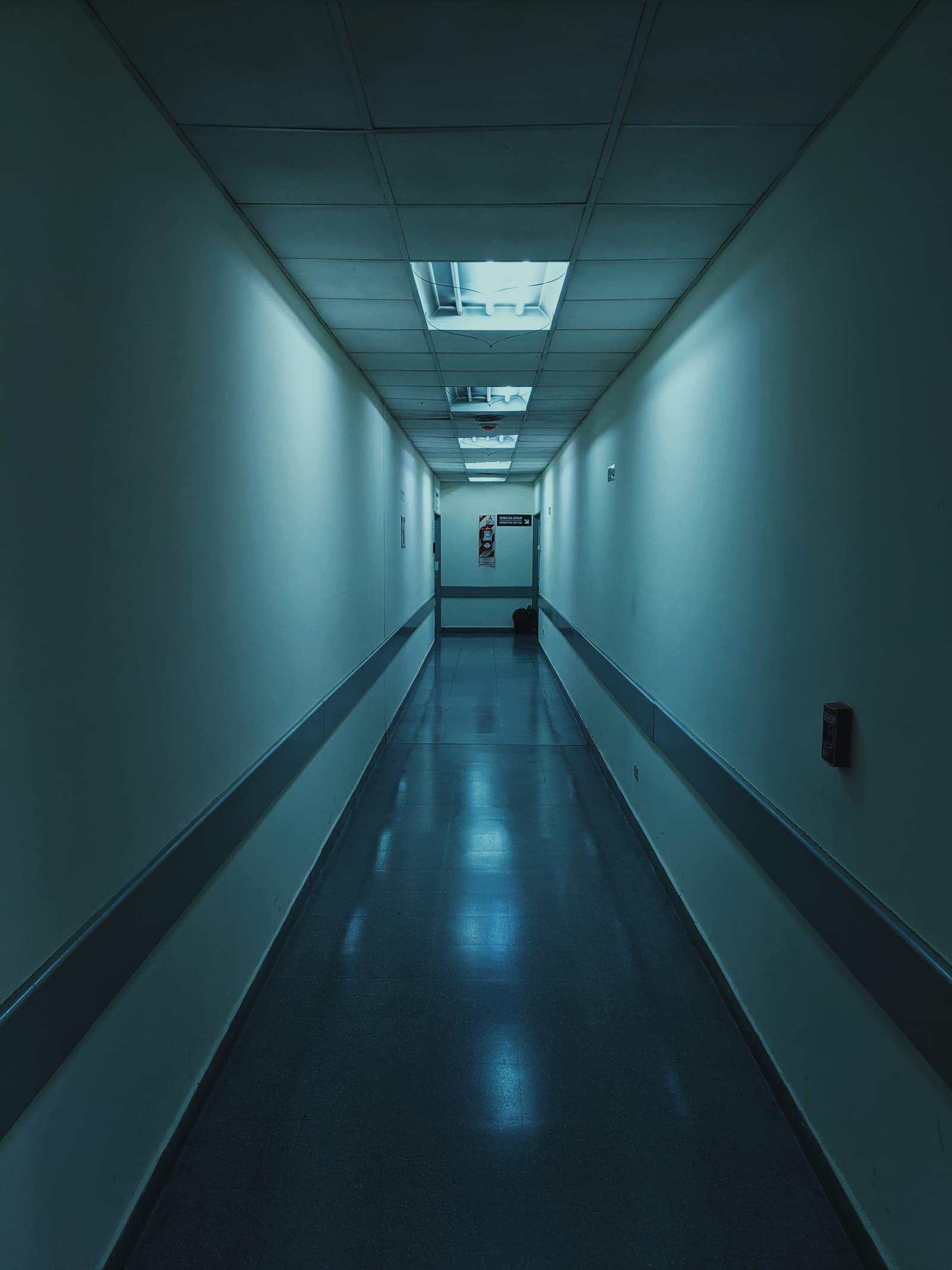 An empty hospital corridor receding under fluorescent light.