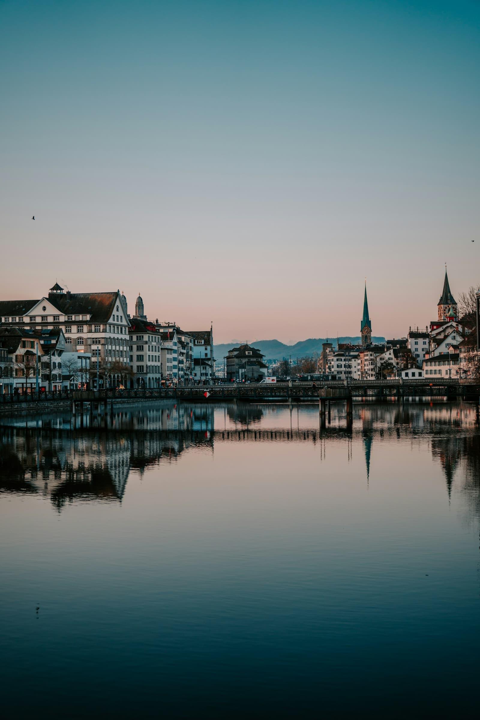 The Limmat riverfront in Zürich at dusk, the old town reflected in the water.
